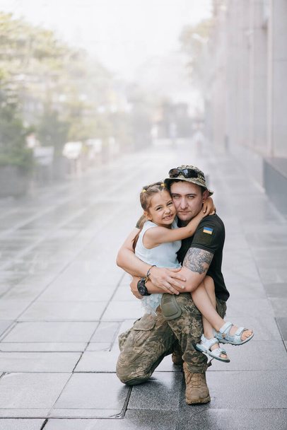 Little Ukrainian girl meets her father from the war during his vacation and joyful embraces him. War in Ukraine. Russian military invasion in Ukraine. War and children. - Photo, Image