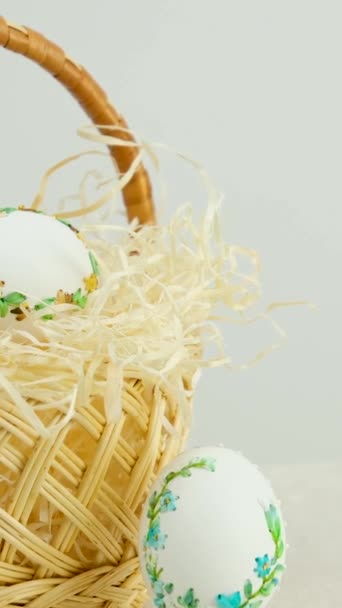 Easter holiday decorative handmade eggs in wicker basket on white table white background embroidery ribbons on eggs ornament blue green yellow color postcard gift congratulations invitation - Imágenes, Vídeo