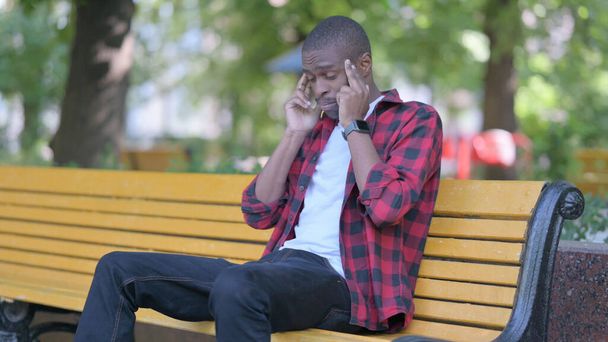 Cansado jovem africano sentado ao ar livre com dor de cabeça - Foto, Imagem