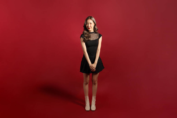 La donna asiatica con il colore nero vestita in piedi sullo sfondo rosso. - Foto, immagini