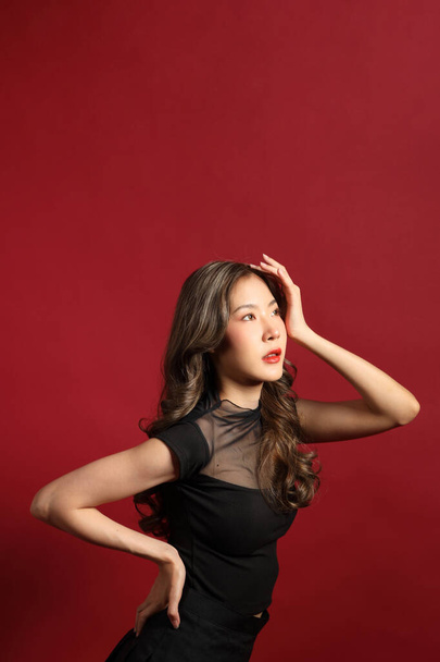 La femme asiatique avec la couleur noire habillée debout sur le fond rouge. - Photo, image