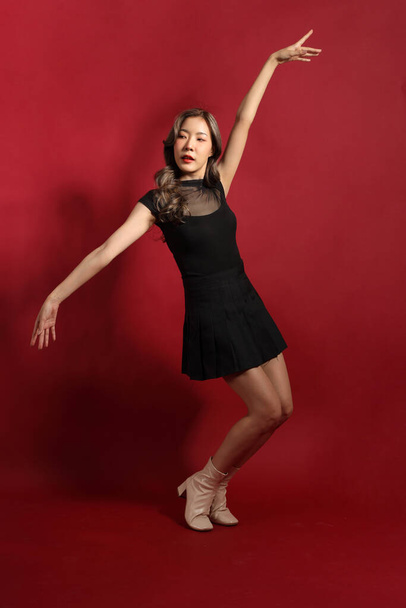 Азиатка с черным цветом одежды, стоящая на красном фоне. - Фото, изображение