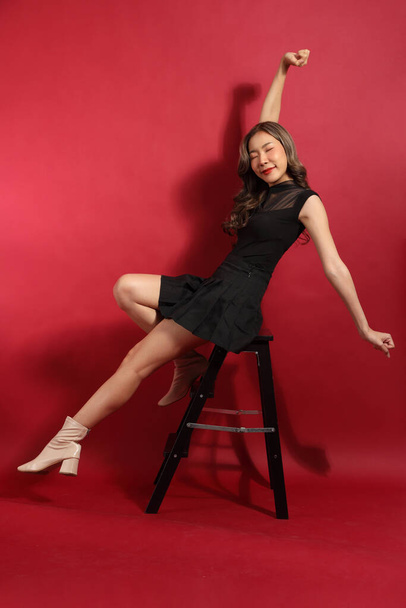 Азиатка с черным цветом одежды сидит на красном фоне. - Фото, изображение