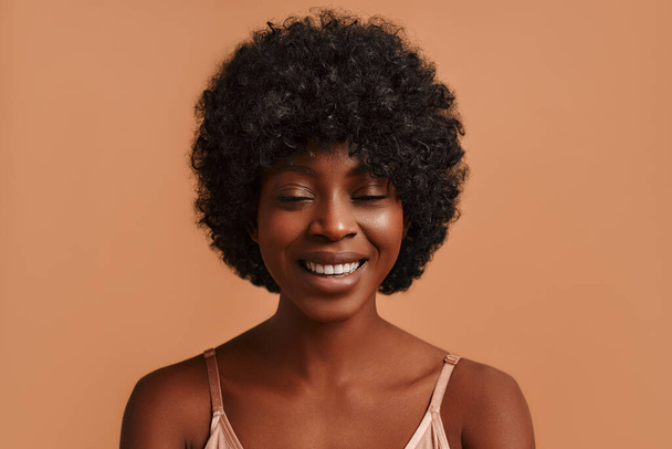 Portret van een jonge Afro-Amerikaanse vrouw in beige lingerie die poseert op een beige achtergrond. Het concept van huidverzorging, cosmetologie en spabehandelingen. - Foto, afbeelding