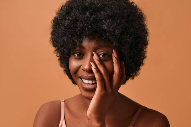 Bej rengi iç çamaşırlı, bej arka planda poz veren Afro-Amerikan bir kadının portresi. Cilt bakımı, kozmetoloji ve kaplıca tedavisi kavramı. - Fotoğraf, Görsel