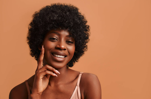 Portrait of a young African-American woman in beige lingerie posing on a beige background. The concept of skin care, cosmetology and spa treatments. - Photo, Image