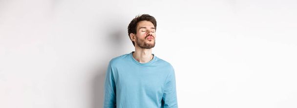 Image of cute and silly man waiting for kiss, pucker lips with closed eyes, standing over white background. - Photo, Image