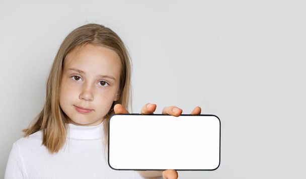 Χαριτωμένο κορίτσι παιδί κρατώντας μεγάλο κενό smartphone με κενή οθόνη λευκό οθόνη για τη νέα εφαρμογή ή το κινητό ιστοσελίδα, Mockup banner - Φωτογραφία, εικόνα
