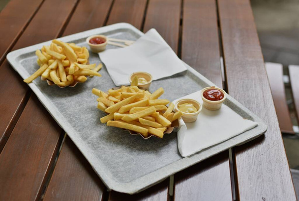 frietjes met ketchup, mayonaise en mosterd op een dienblad op een houten statief - Foto, afbeelding