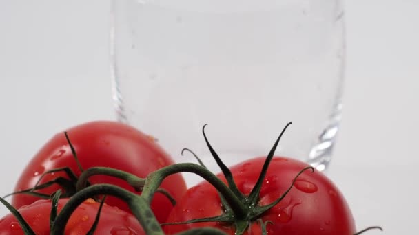 Le jus de tomate est versé dans un verre. Jus de tomate fraîchement préparé et tomates sur fond blanc. Zoom caméra. - Séquence, vidéo