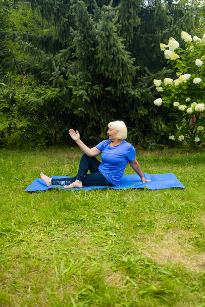Lekkoatletyczna kobieta po 50. roku życia pozuje na macie do jogi na świeżym powietrzu ubrana w stroje sportowe sama w parku lub w lesie w przyrodzie. Wysokiej jakości zdjęcie - Zdjęcie, obraz