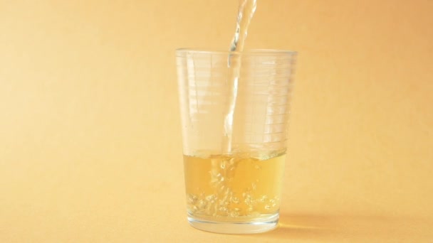 Echar jugo de naranja en un vaso sobre un fondo de color , - Metraje, vídeo