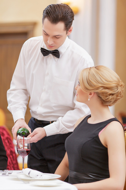 Waiter serving wine to his beautiful female client - Фото, изображение