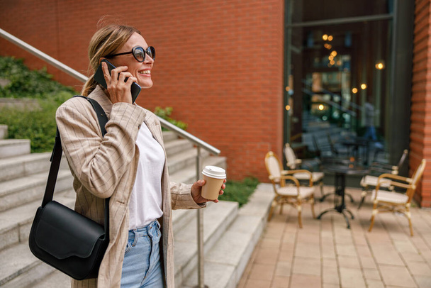 Smiling woman office worker is talking by phone while standing on modern building background  - Foto, immagini