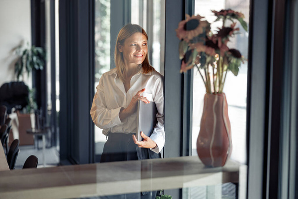 Femme d'affaires debout avec ordinateur portable en coworking et en regardant côté. Concept de travail à distance - Photo, image