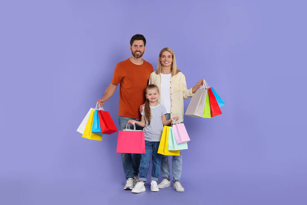 Family shopping. Happy parents and daughter with many colorful bags on violet background - Foto, Bild