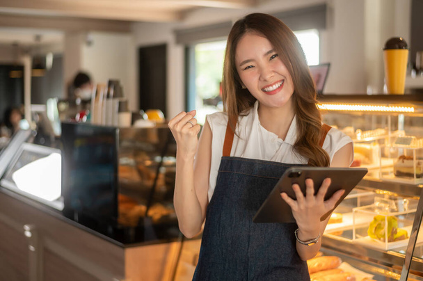 An Asian woman entrepreneur using tablet checking stock or sale income in modern coffee shop , concept small business  - Foto, Imagem