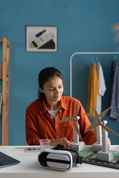 Vrouwelijke architect in haar thuiskantoor werkt met duurzame energie project met model windturbines. Kopieerruimte - Foto, afbeelding