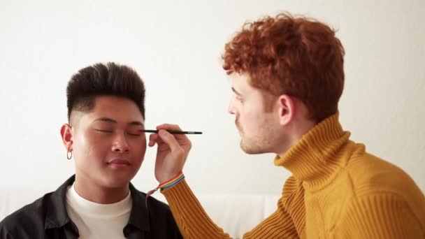 cámara lenta video de un concentrado gay hombre aplicación maquillaje a su pareja en casa - Imágenes, Vídeo