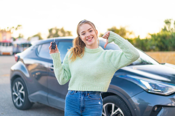 Młoda ładna dziewczyna trzyma kluczyki do samochodu na zewnątrz dumny i zadowolony z siebie - Zdjęcie, obraz