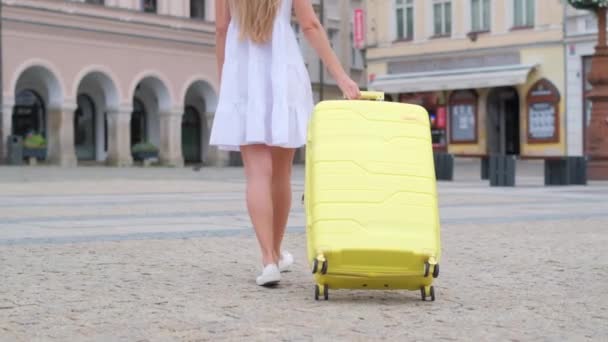 Een vrouw loopt met een gele koffer op straat in een Europese stad, toerisme in Europa. Zomervakantie - Video