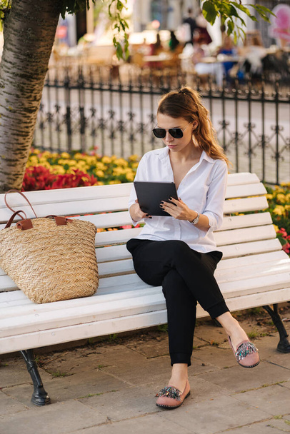 Mujer sentada en el banco en el parque y trabajando usando la tableta. Freelancer femenina. Foto de alta calidad - Foto, Imagen