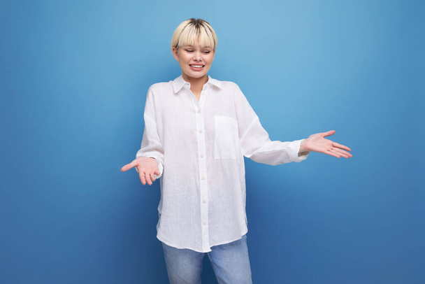 jonge mooie blonde carrière vrouw in een wit shirt poseren op een blauwe achtergrond met kopieerruimte. mensen levensstijl concept. - Foto, afbeelding