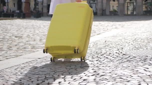 Detailní záběr ženy kráčející po krásné ulici s turistickým kufříkem na pozadí slunečních paprsků. - Záběry, video