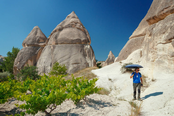Homem com guarda-chuva caminhando entre formações geológicas únicas na Capadócia contra o céu azul no verão. Popular área turística em Goreme, Nevsehir, Turke - Foto, Imagem