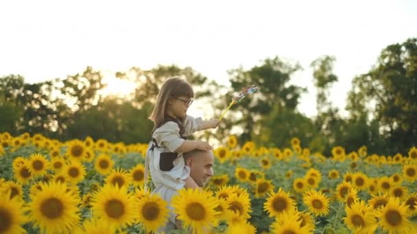 Ein Vater trägt seine Tochter mit Down-Syndrom im Sommer auf den Schultern in einem Sonnenblumenfeld. - Filmmaterial, Video