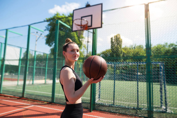 Молодая спортивная девушка с баскетбольным мячом на баскетбольной площадке на открытом воздухе, активные выходные. - Фото, изображение