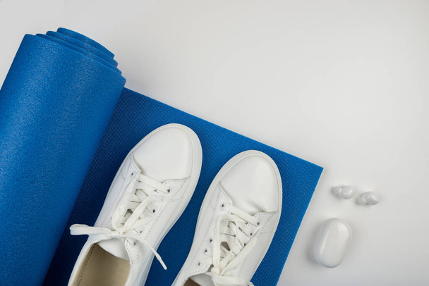 Fitness concetto accessori. Foto di manubri, smartphone con cuffie bianche sneakers sportive mat su sfondo bianco con spazio vuoto. - Foto, immagini
