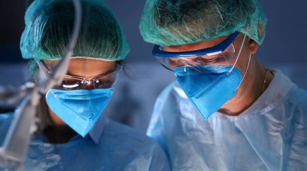 Lähikuva vakavista kirurgeista sinisissä naamareissa leikkaussalissa. Lääkäri lääkärin lasit avustavat prosessin aikana. Lääketieteen ja terveydenhuollon käsite
 - Valokuva, kuva