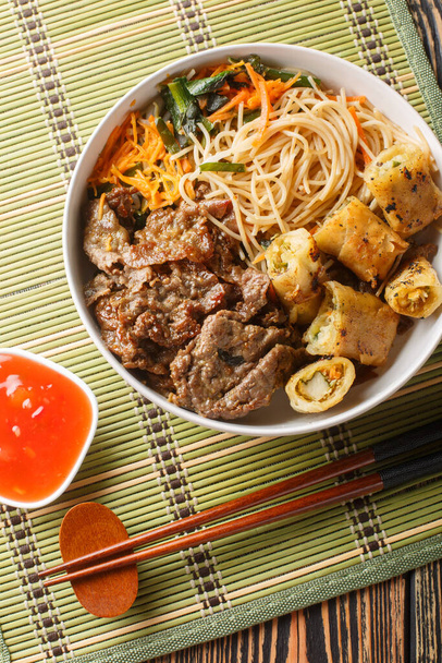 Vietnámi saláta marhahúsból, rizspogácsából, zöldségekből és sült tavaszi tekercsekből az asztalon. Függőleges felülnézet abov-tól - Fotó, kép