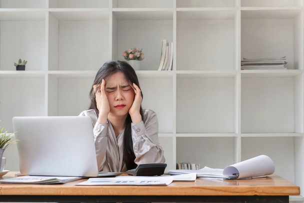 Zakenvrouw ziet er gestrest uit terwijl ze in een kantoor werkt. Gestresste zakenvrouw werken vanaf op laptop kijken bezorgd, moe en overweldigd. - Foto, afbeelding