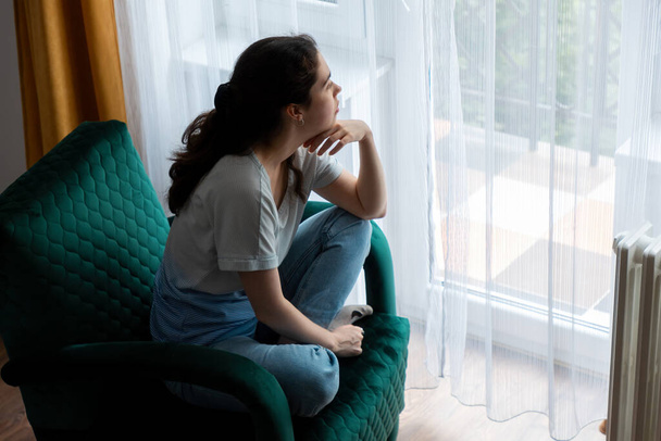 Widok z góry na młodą białą kobietę siedzącą na zielonym welurowym fotelu i patrzącą w okno. Pojęcie depresji, psychologii i problemów psychicznych. - Zdjęcie, obraz