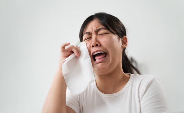 Ritratto di una donna asiatica triste che piange si asciuga le lacrime con un asciugamano di carta velina. - Foto, immagini