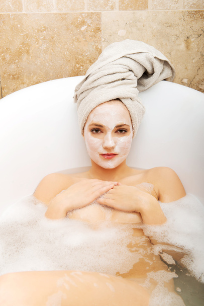 Woman relaxing in bathtub with face mask. - Фото, зображення