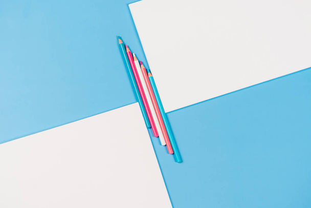 Due quaderni bianchi con matite di colore azzurro, rosa, bianco tra su fondo azzurro. Vista dall'alto, copia lo spazio per il testo. - Foto, immagini