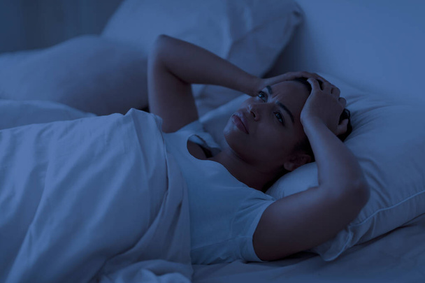 Πρόβλημα ύπνου. Αγχωμένη Αφροαμερικανή ξαπλωμένη μόνη στο κρεβάτι και αγγίζοντας το κεφάλι, νεαρή μαύρη γυναίκα ξύπνια τη νύχτα, να νιώθει κατάθλιψη, να υποφέρει από αϋπνία ή ψυχικά προβλήματα - Φωτογραφία, εικόνα