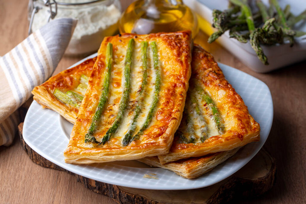 Baked green asparagus with ham and cheese in puff pastry sprinkled with sesame seeds and green basil leaves.  - Foto, Imagen