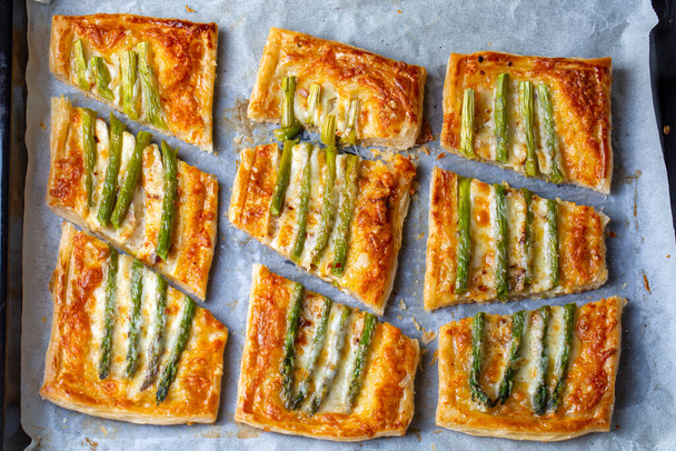 Baked green asparagus with ham and cheese in puff pastry sprinkled with sesame seeds and green basil leaves.  - Foto, Bild