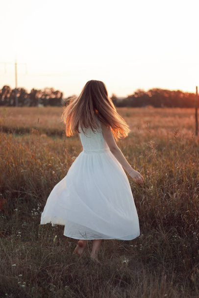 Kaunis tyttö tanssii pellolla auringonlaskun aikaan valkoisessa mekossa. Onnellinen nainen Konsepti. Morsian - Valokuva, kuva