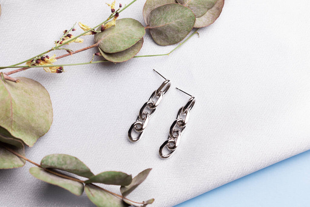 Creatieve compositie met eenvoudige zilveren sieraden oorbellen gezet op zijde achtergrond met gedroogde bloemen. Trendy handgemaakte accessoires in minimalistische stijl - Foto, afbeelding