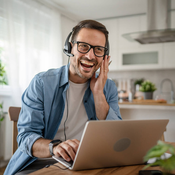 Egy férfi kaukázusi férfi szabadúszó munka otthonról fejhallgatóval a fején laptop számítógép ügyfélszolgálat diszpécser boldog mosoly magabiztos - Fotó, kép