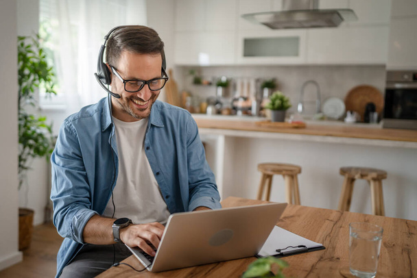 Egy férfi kaukázusi férfi szabadúszó munka otthonról fejhallgatóval a fején laptop számítógép ügyfélszolgálat diszpécser boldog mosoly magabiztos - Fotó, kép