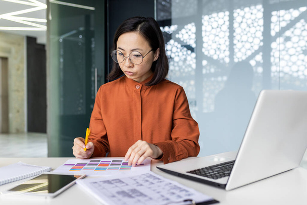 Serious thinking female financier on paper work, Asian concentrated writing data in forms, using laptop at work, reviewing contracts financial reports, accountant at workplace. - Photo, Image