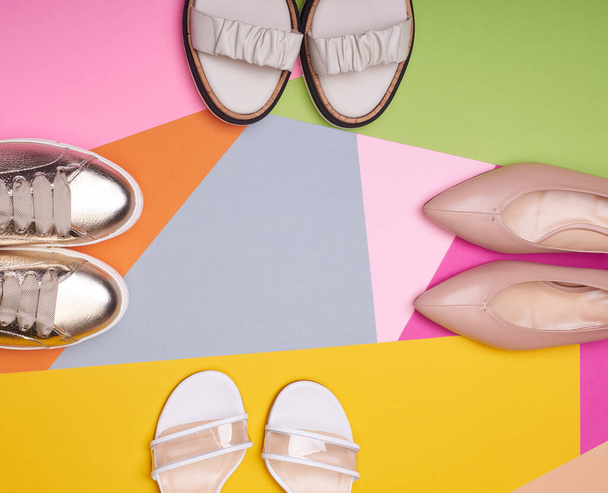 Čtyři páry různých stylových dámských bot na vícebarevném pozadí. Byt ležel, horní pohled, kopírovací prostor uprostřed. Reklamní plakát. Módní blog nebo časopis koncept. Balení pro letní cestovní koncept - Fotografie, Obrázek