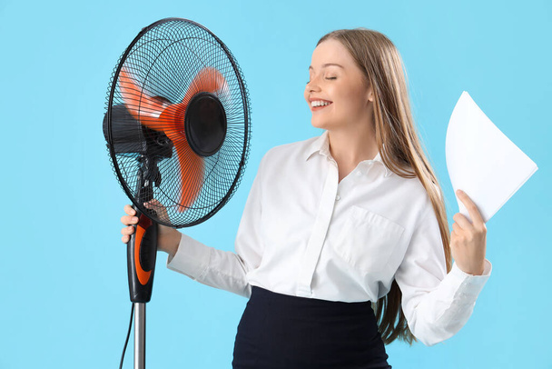 Giovane donna d'affari con carte e ventilatore elettrico su sfondo blu - Foto, immagini