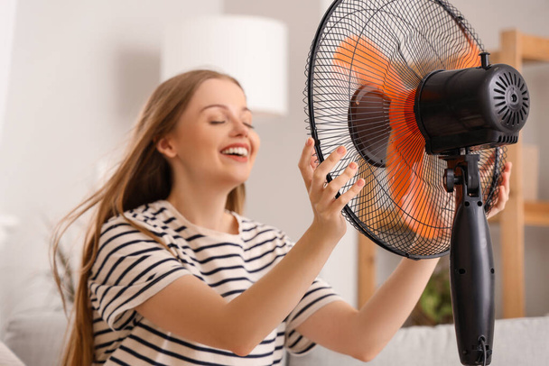 Mladá žena s foukající elektrický ventilátor doma - Fotografie, Obrázek